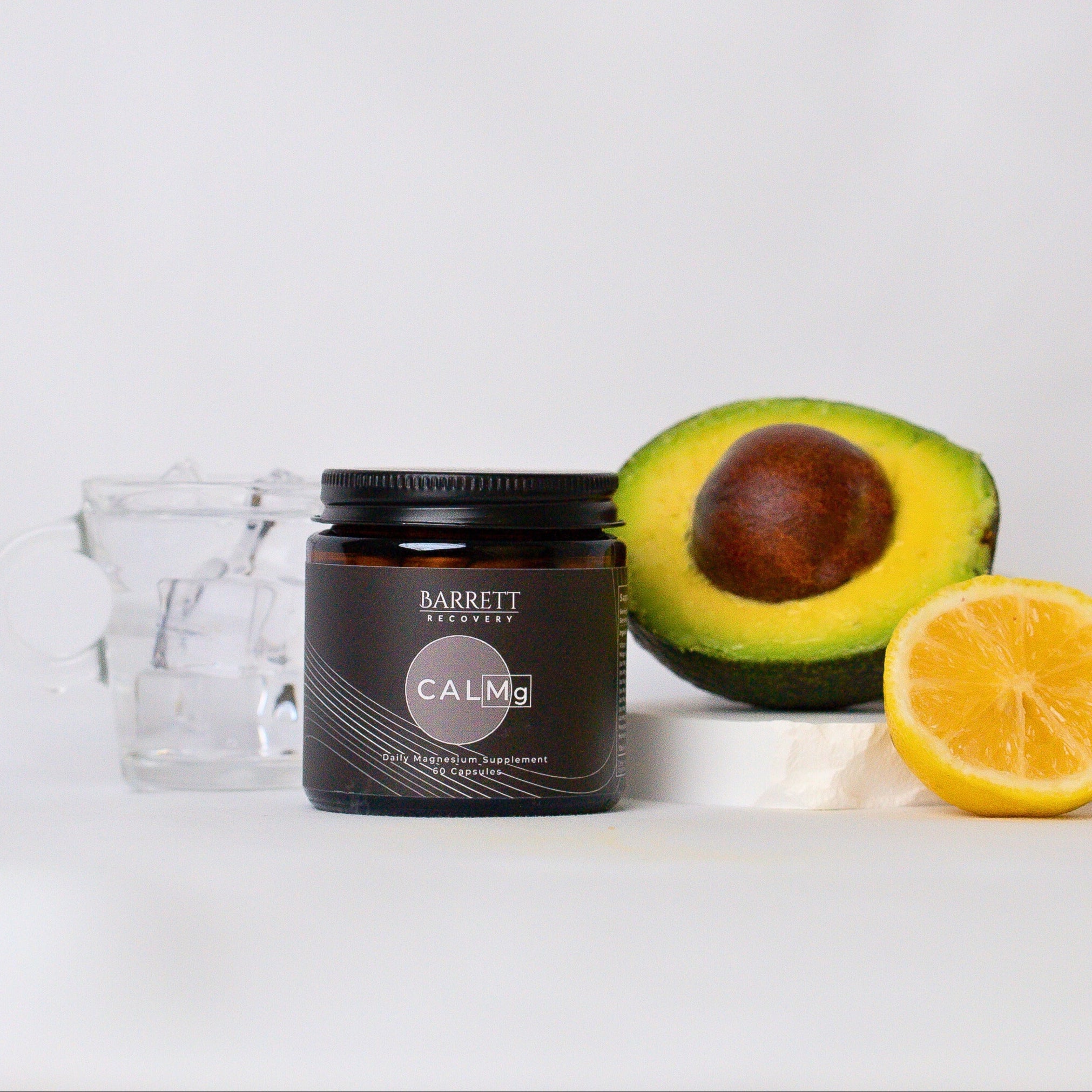 Calmg Daily magnesium supplement next to a glass of water, avocado, and lemon